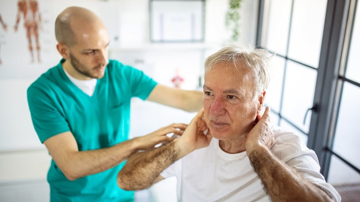 Medical professional examines a senior man who has neck pain.