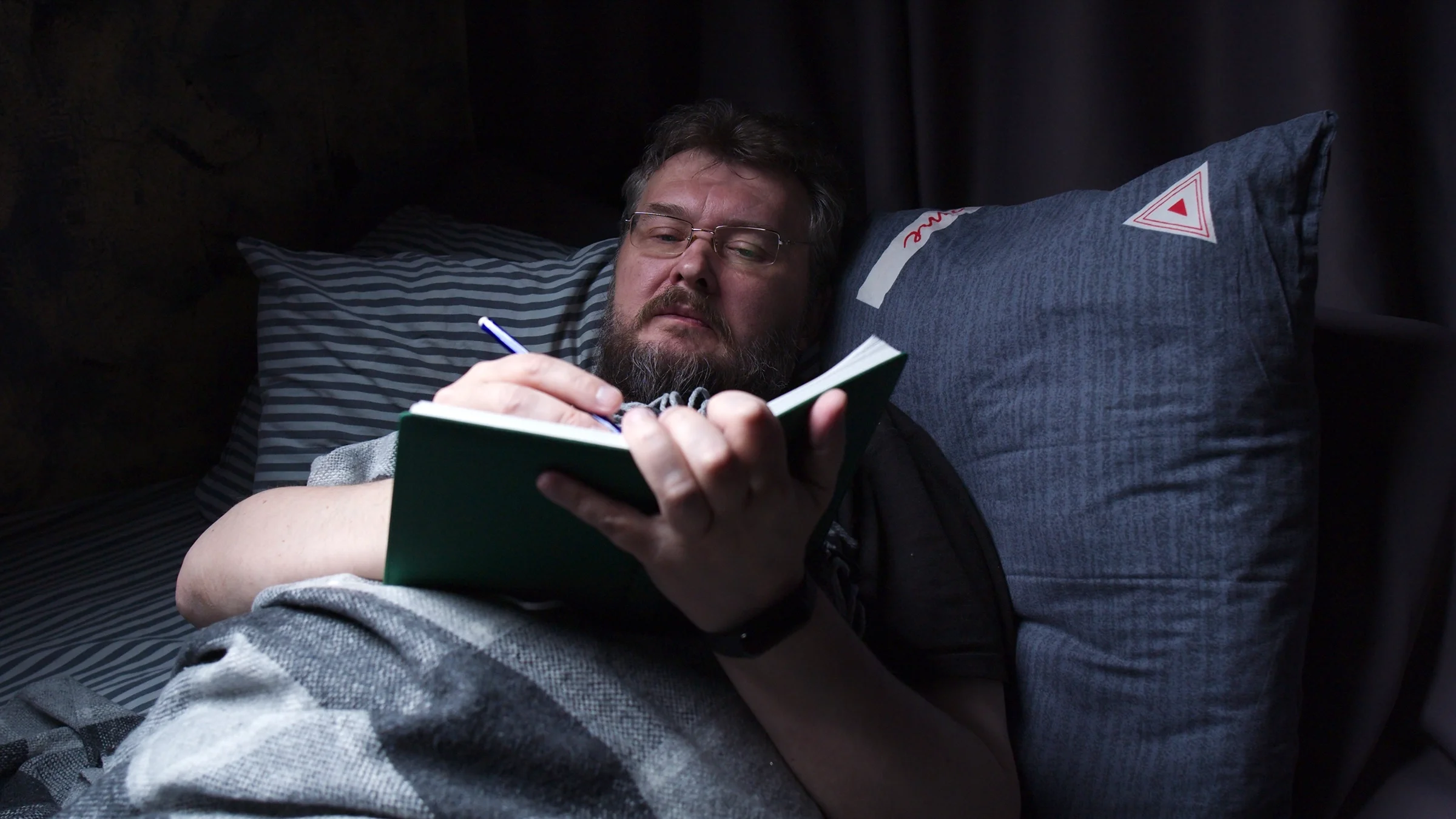 Man writing in his journal while laying in bed before sleep.