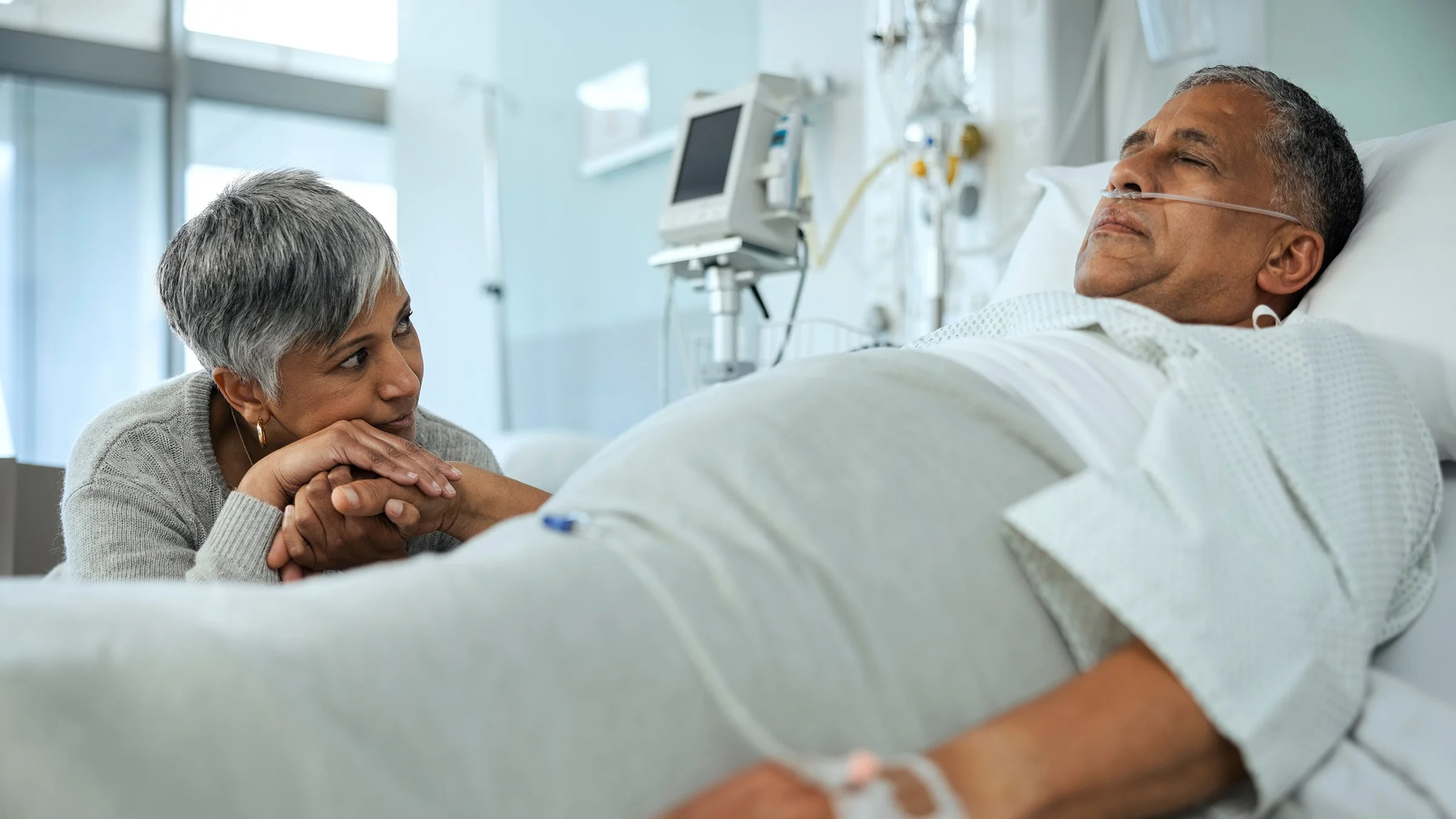 Woman holds hand with senior man at his hospital bedside