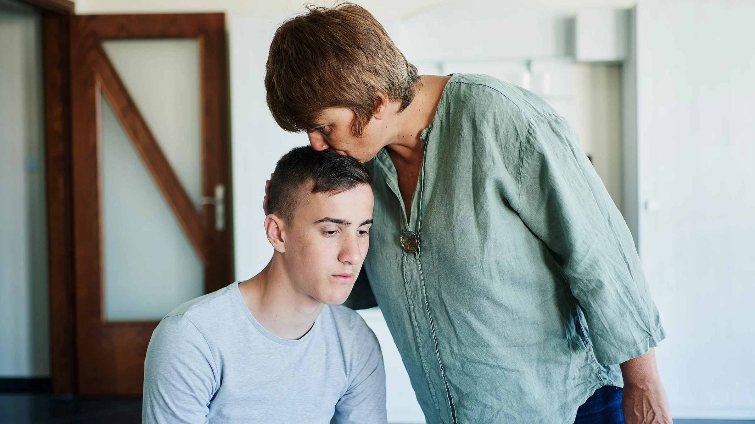 Mother bending over to kiss her son on the head.