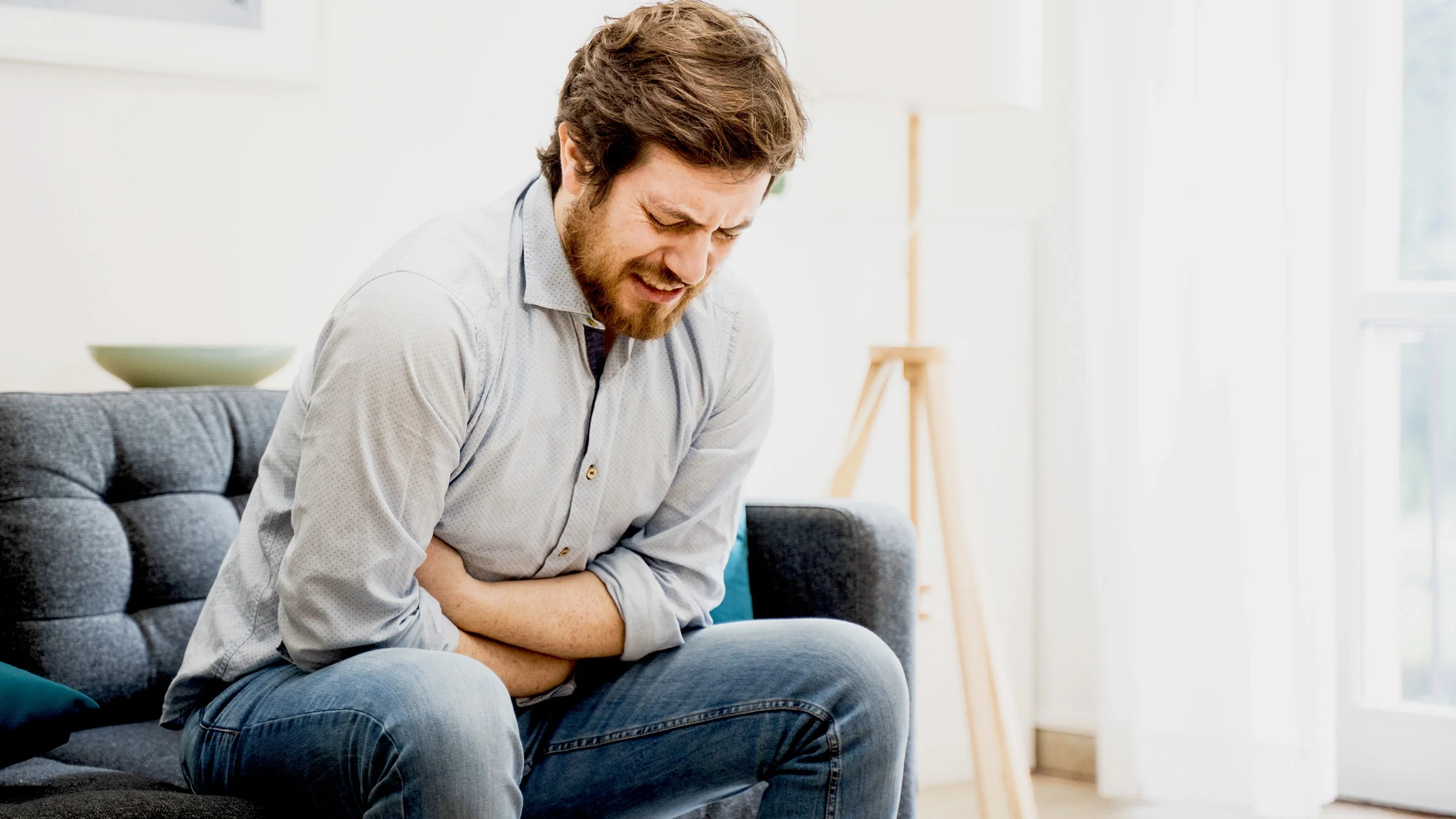 A person experiencing stomach pain on their couch.