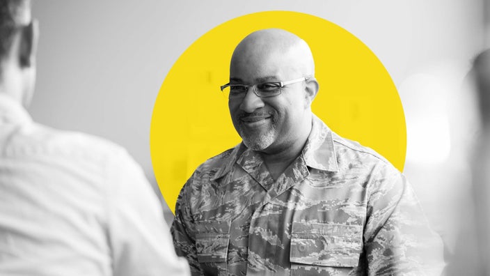 Military man at a doctors check-up in an exam room. He is wearing glasses and smiling.