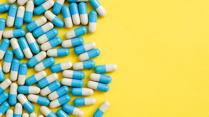 Blue and white oblong pill capsules on the left side on a bright yellow background.