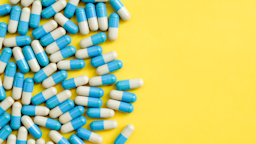 Blue and white oblong pill capsules on the left side on a bright yellow background.
ponsulak/iStock via Getty Images