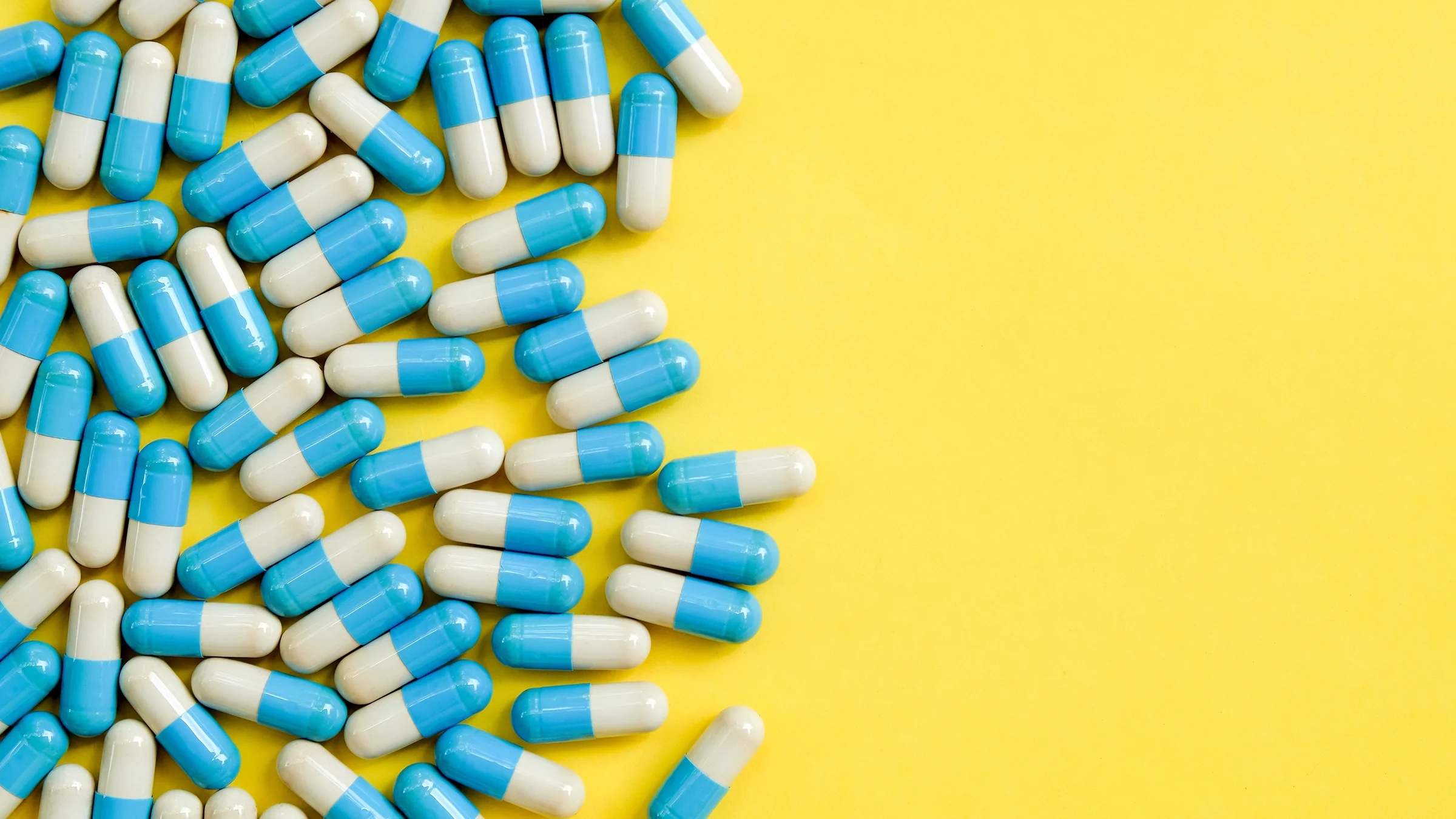 Blue and white oblong pill capsules on the left side on a bright yellow background.