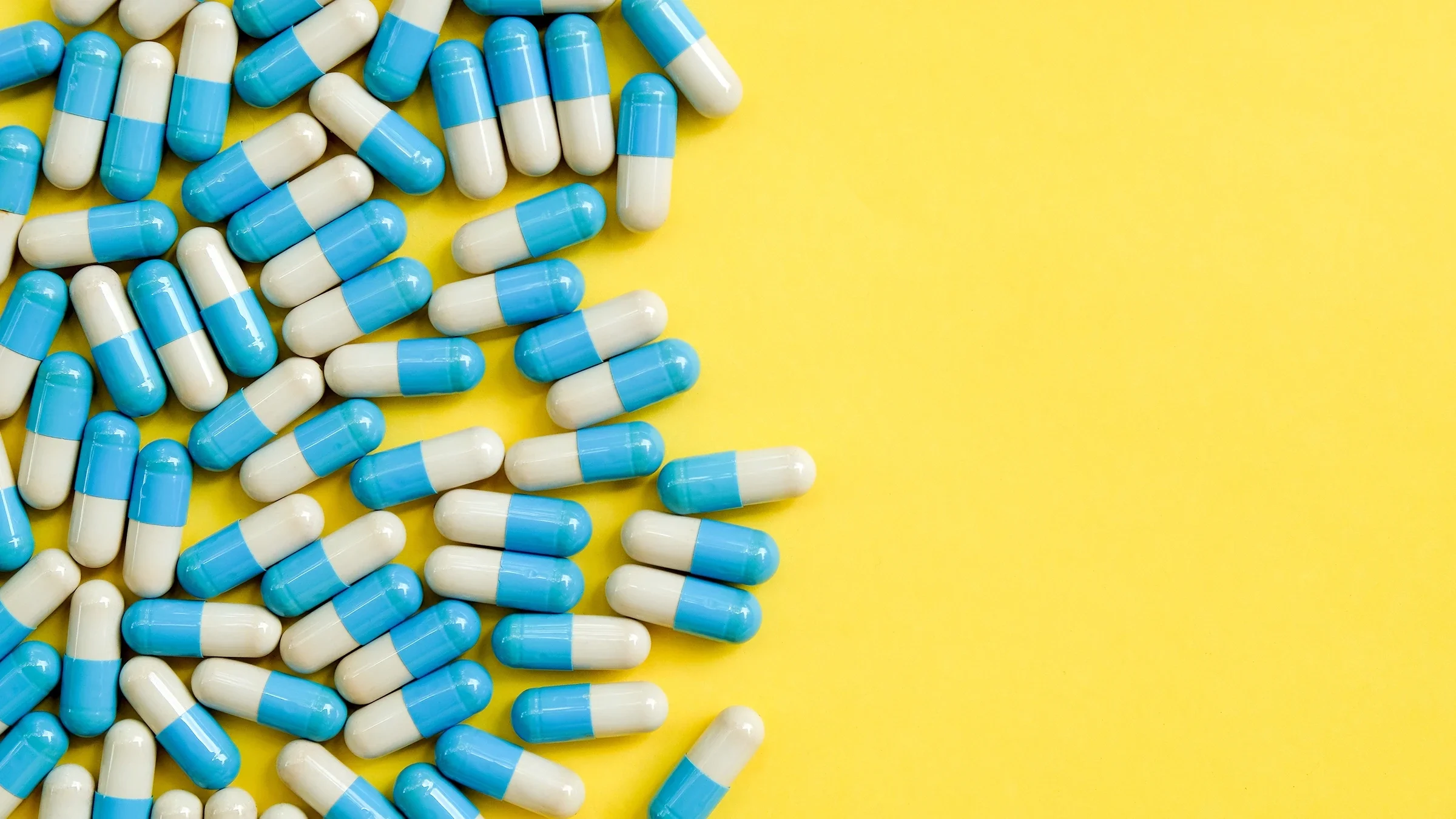 Blue and white oblong pill capsules on the left side on a bright yellow background.