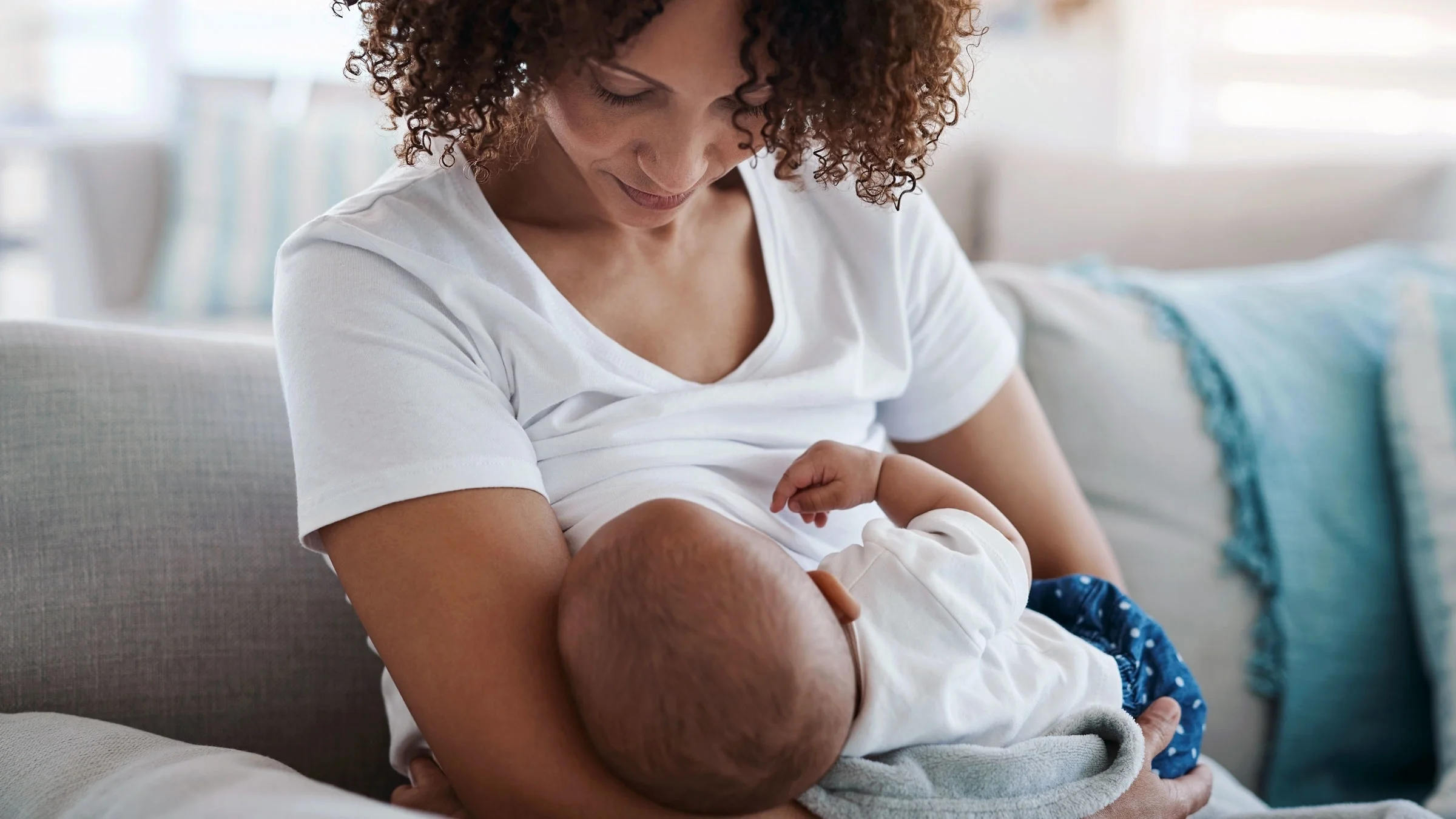 A woman breastfeeds her baby on the sofa at home.