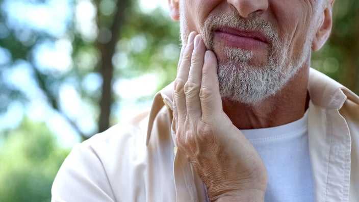 A man is holding his jaw in pain in a closeup. 