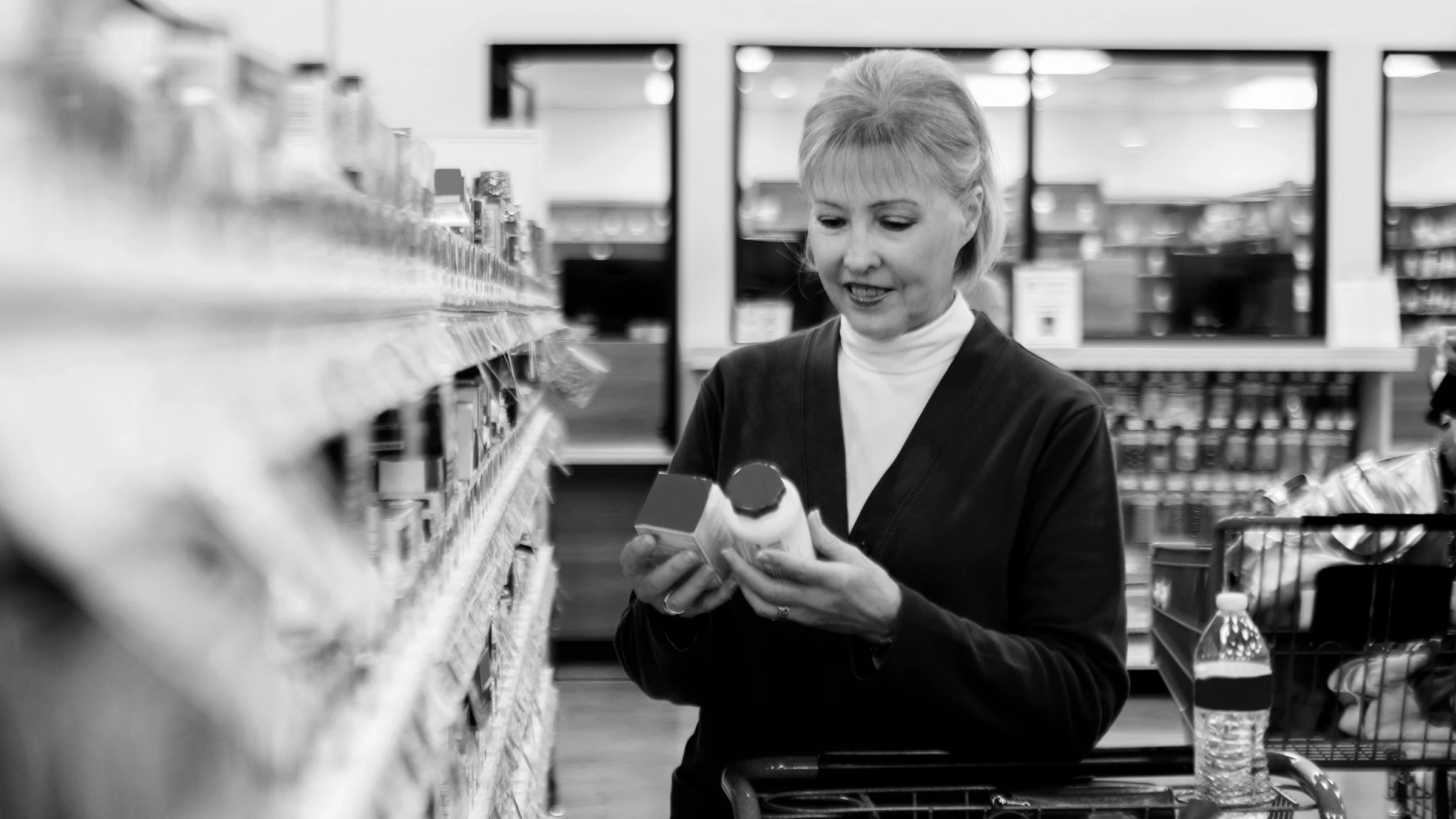 Black and white image of an older woman shopping for medication at the pharmcy.