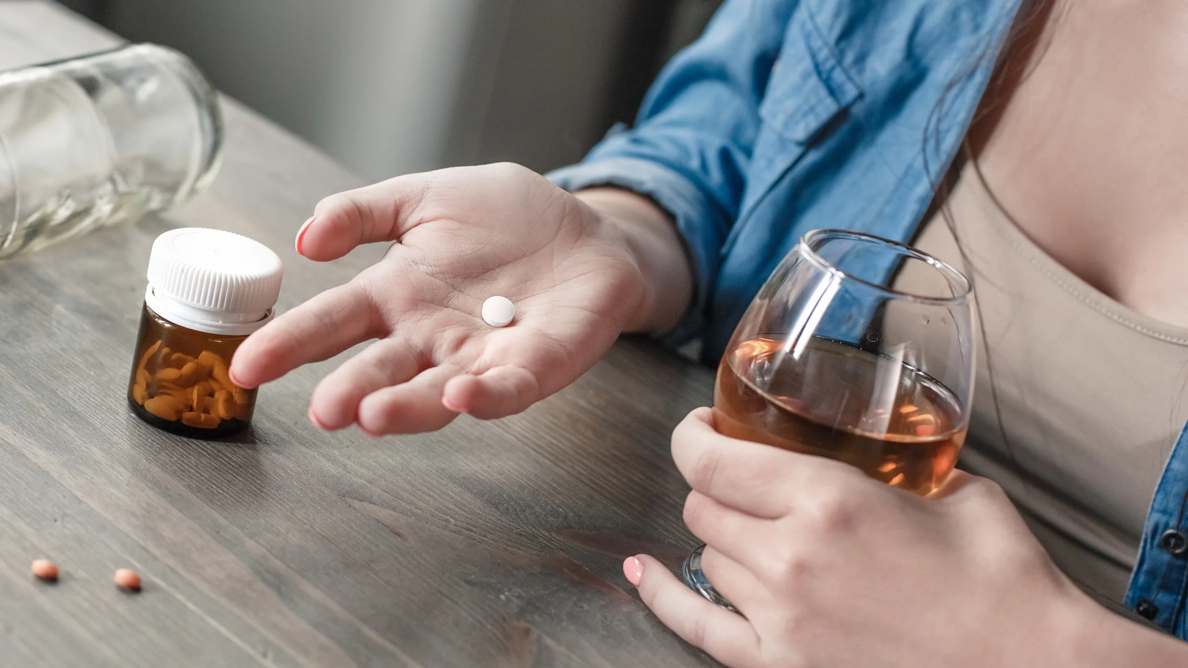 A person holding a pill in one hand and a wine glass in the other.