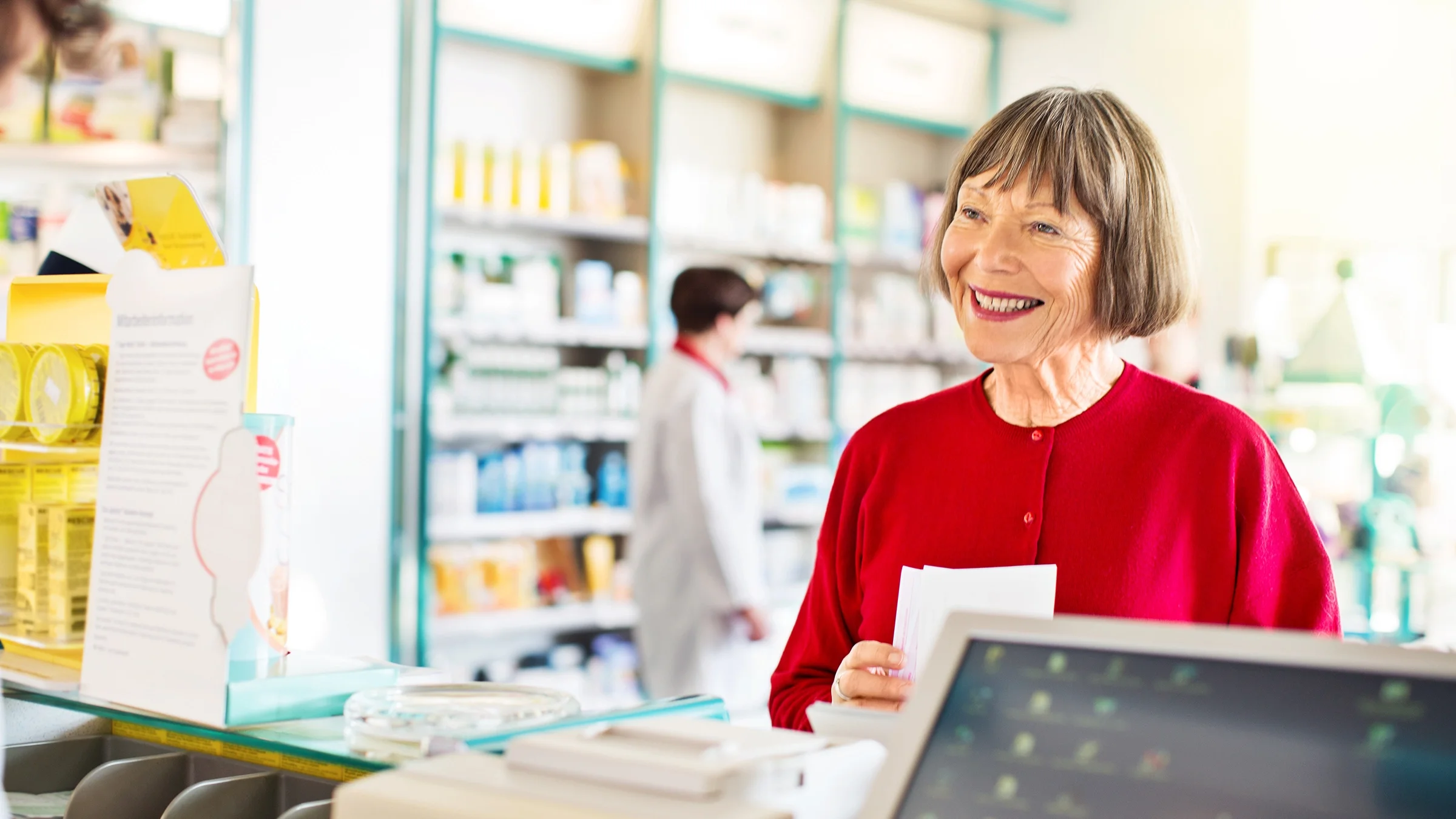 An older woman stands at the pharmacy counter.