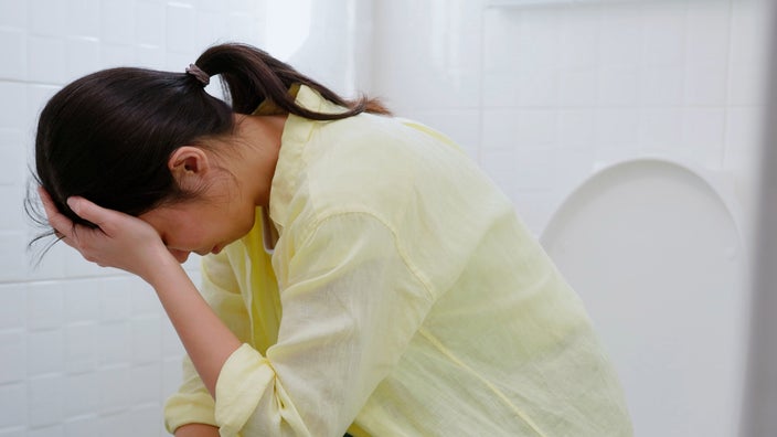 A person sitting on their toilet in pain.