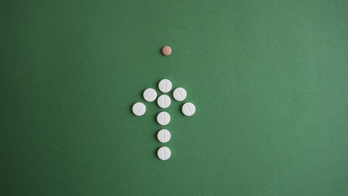 White round pills forming an "up" arrow pointing at a small brownish round pill on dark green background.