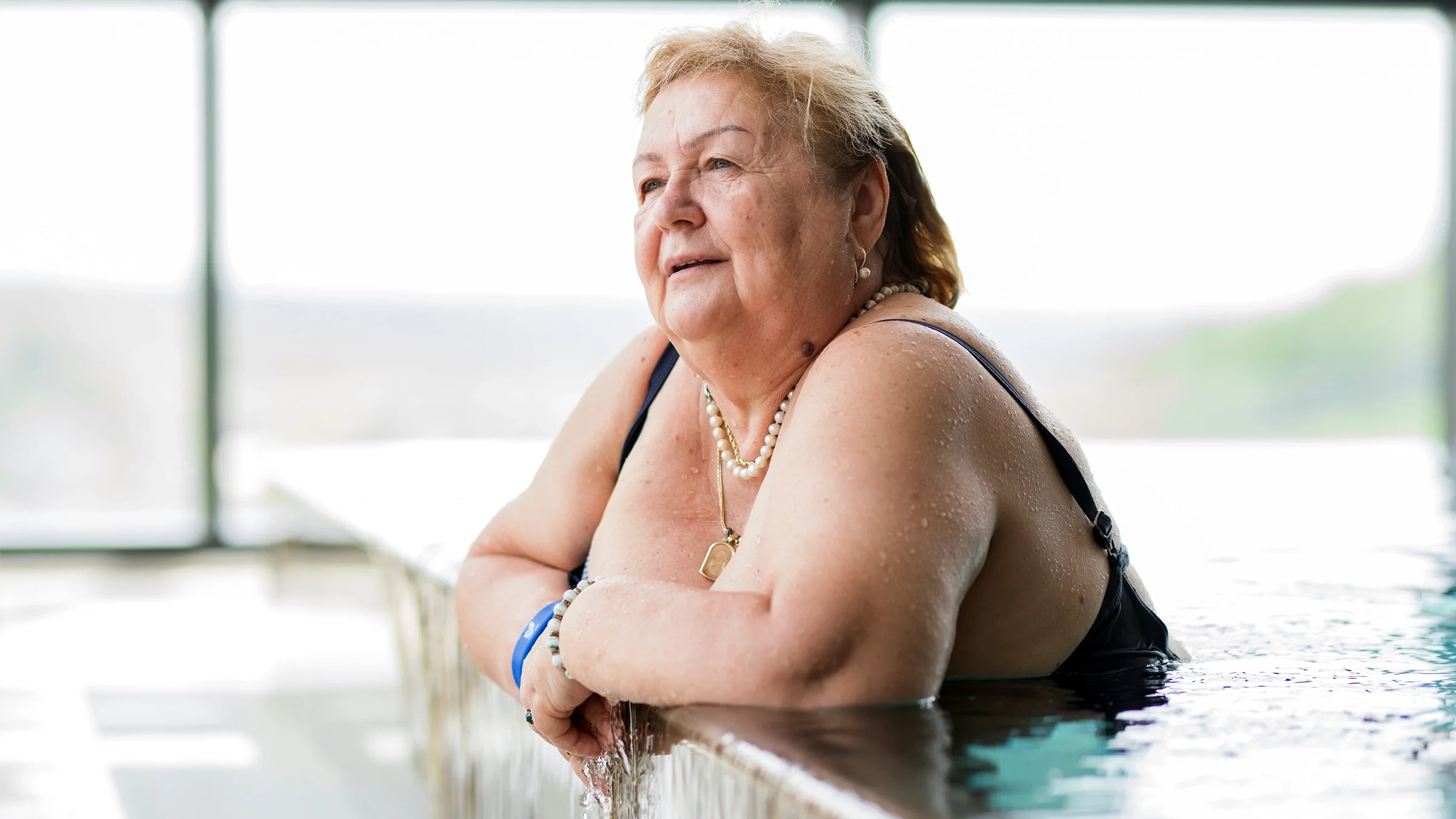 An older woman is relaxing at the edge of a swimming pool.