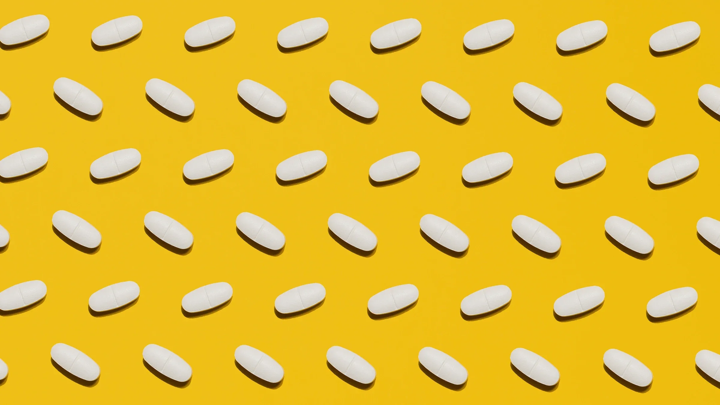 Oblong white pills laid in a pattern on a bright yellow background.
Margarita Kuzniatsova/iStock via Getty Images