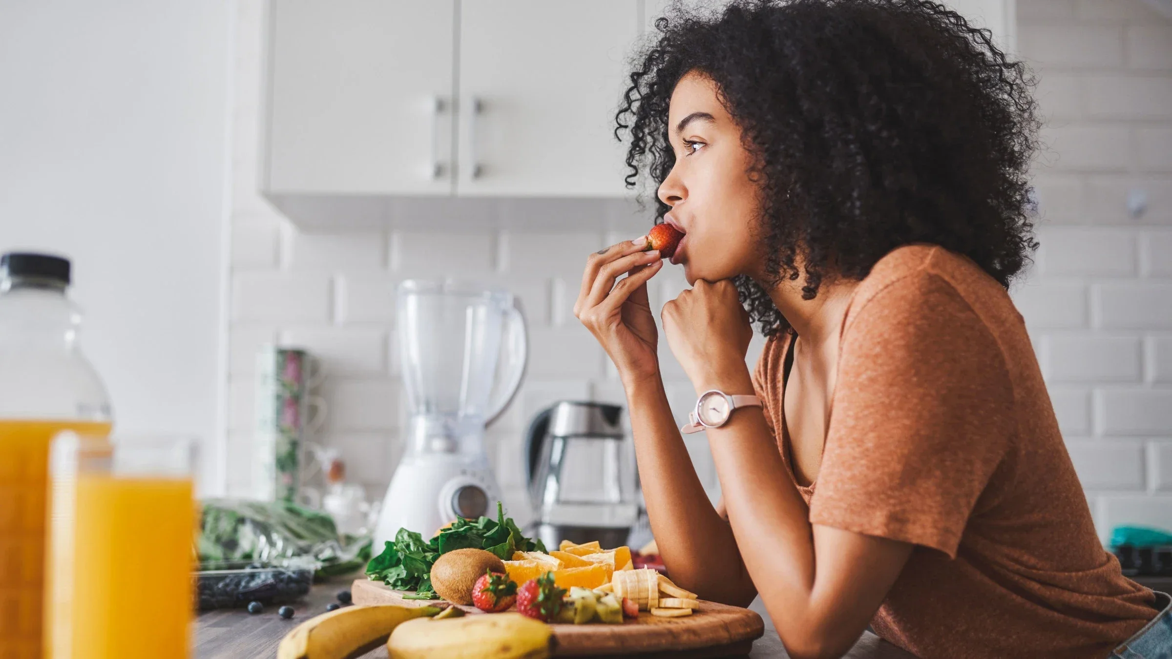 Woman eating fruit at kitchen counter.
Moyo Studio/E+ via Getty Images