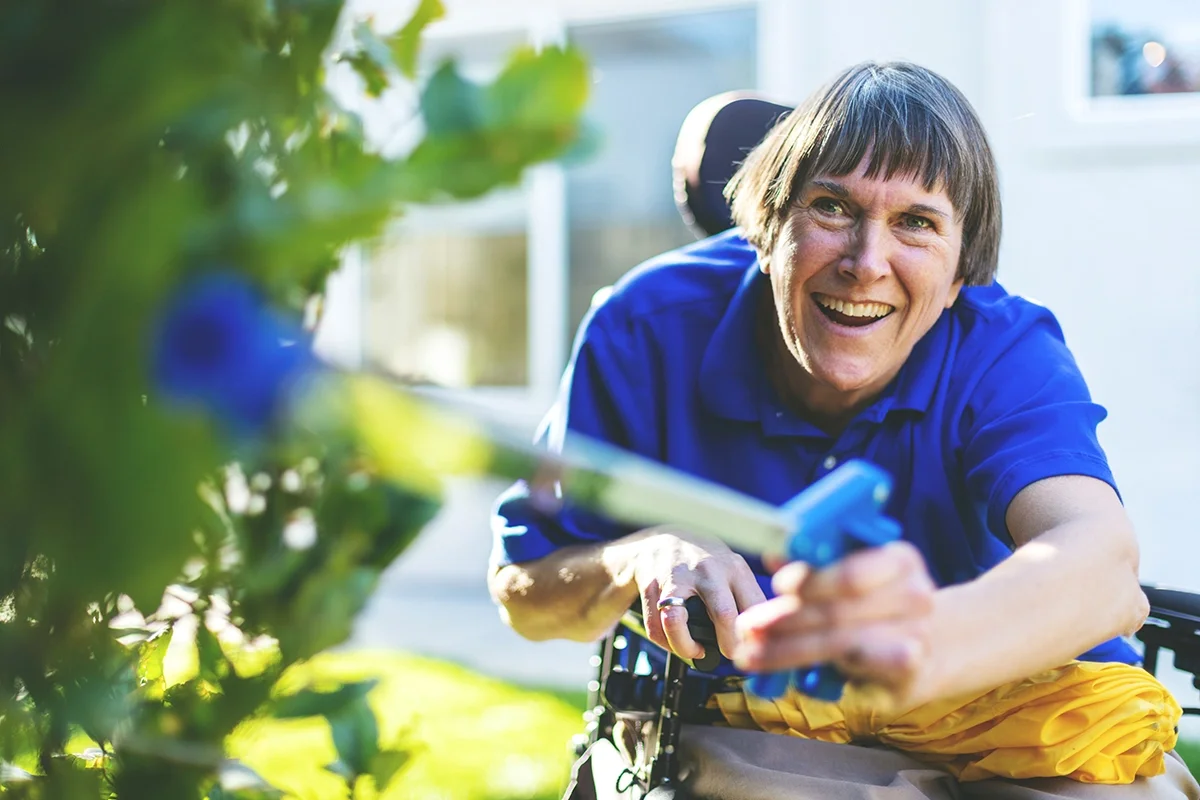 Close-up of a woman using a grabber device to garden while she is in a wheelchair with Multiple Sclerosis (MS).