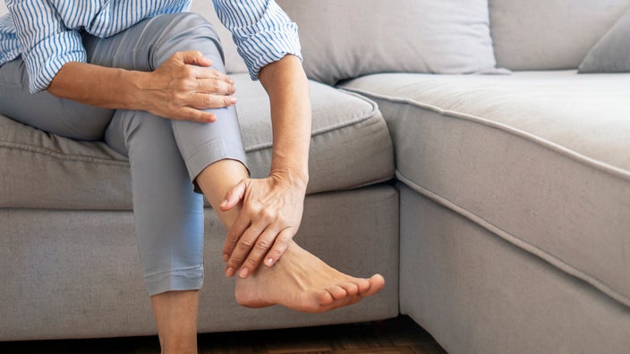 Close-up of a woman rubbing her sore feet. She is sitting a on a gray couch.