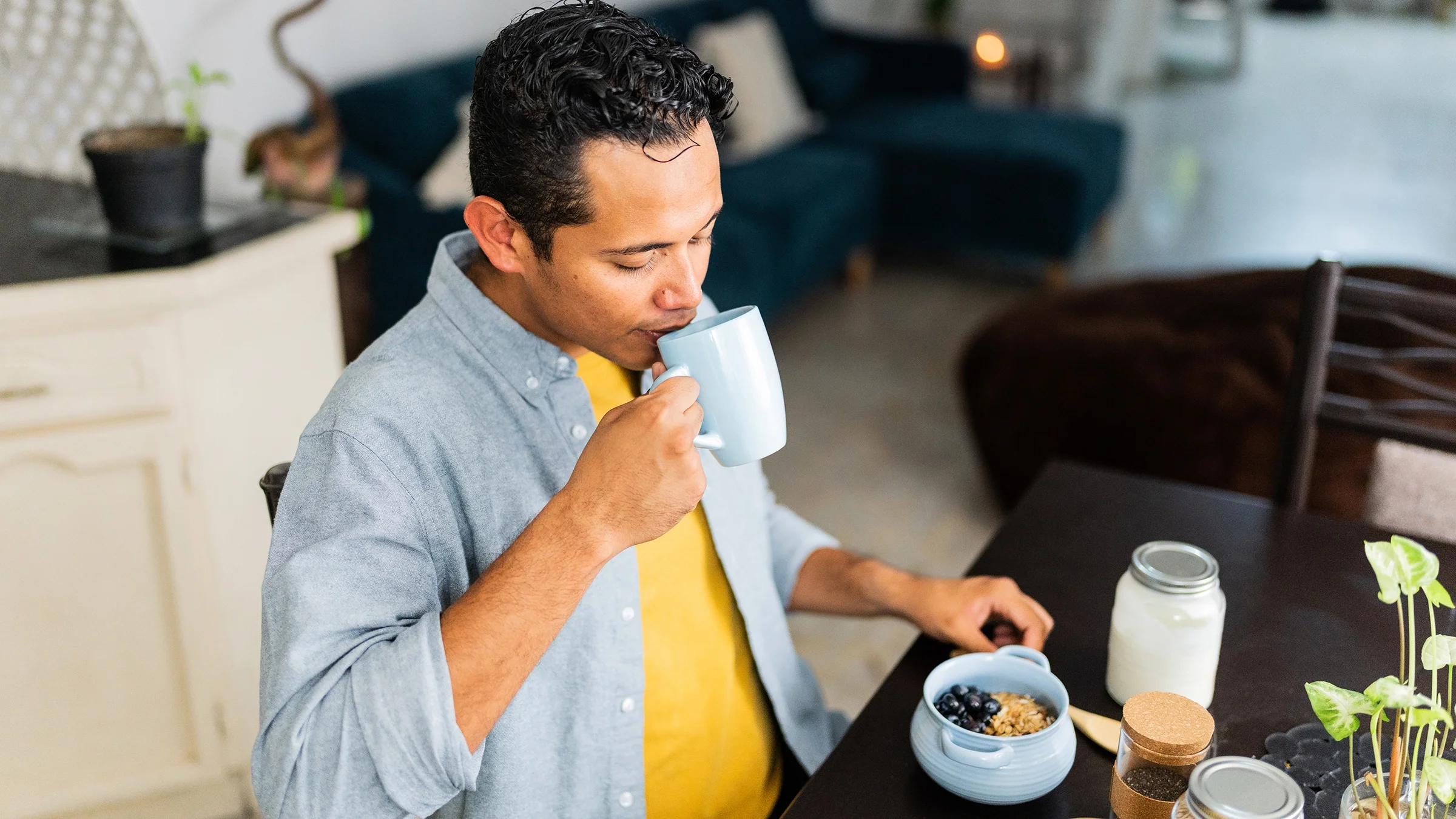 A man takes a drink of coffee during breakfast at home.