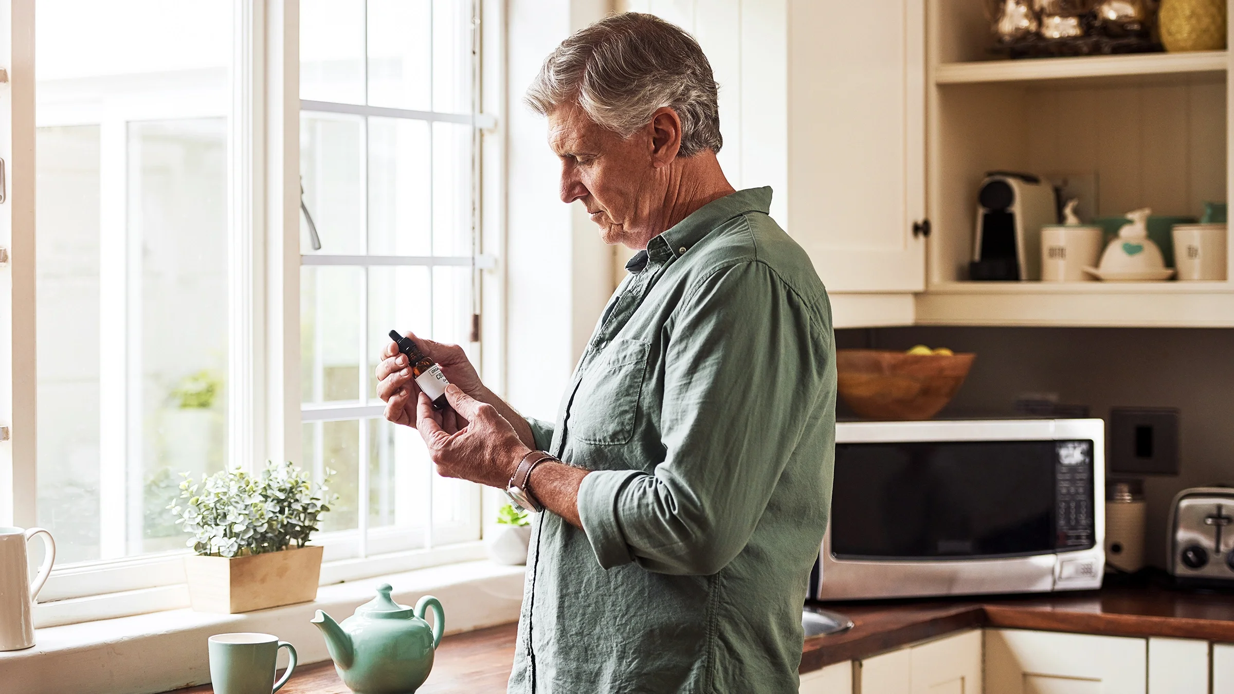 A man prepares to add CBD oil to a cup of tea.