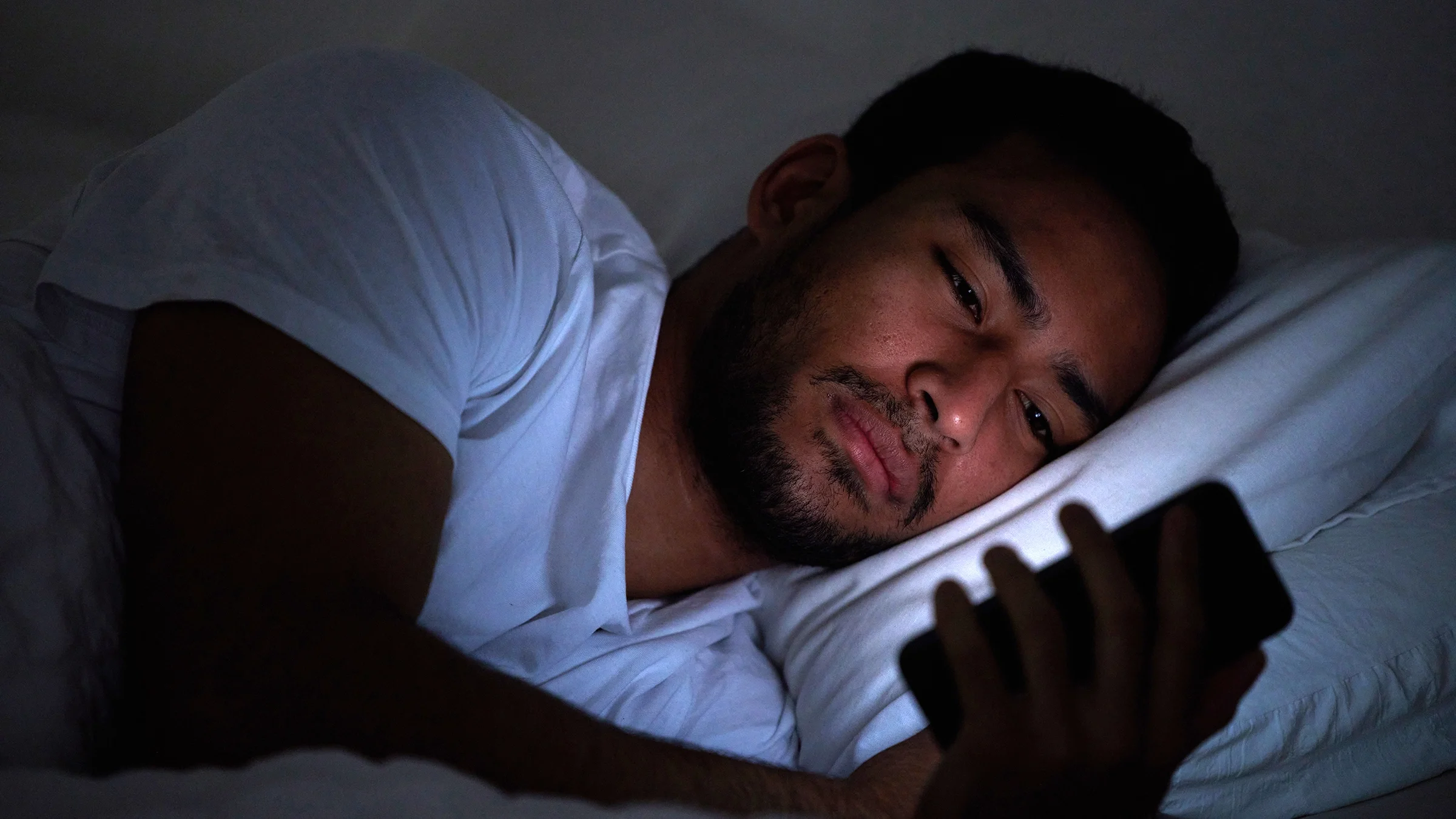 Man staring at a mobile device while lying in bed at night