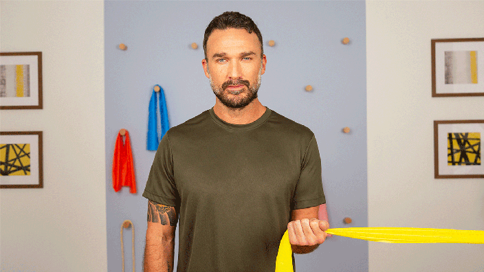 A man demonstrates an internal rotation shoulder exercise by pulling a resistance band with one arm. 