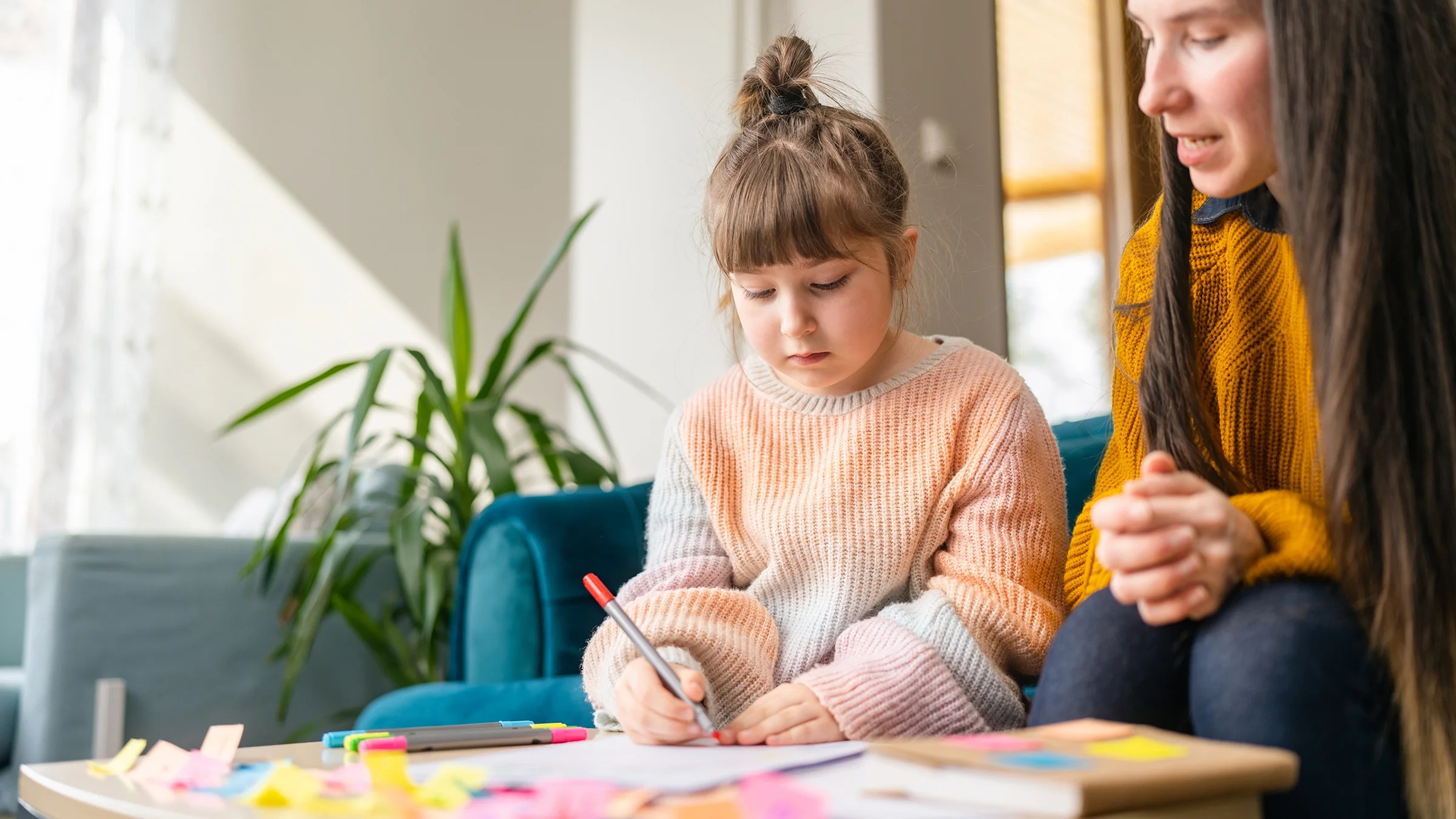 A little girl with an adult is shown. The girl is drawing a picture with markers.