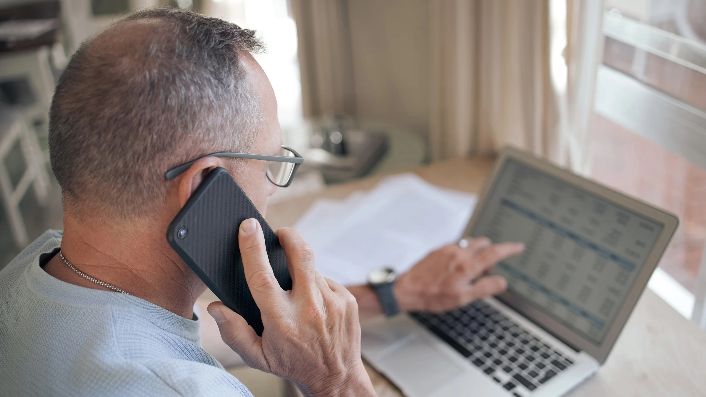 Older man on the phone while reviewing something on his laptop in front of him.