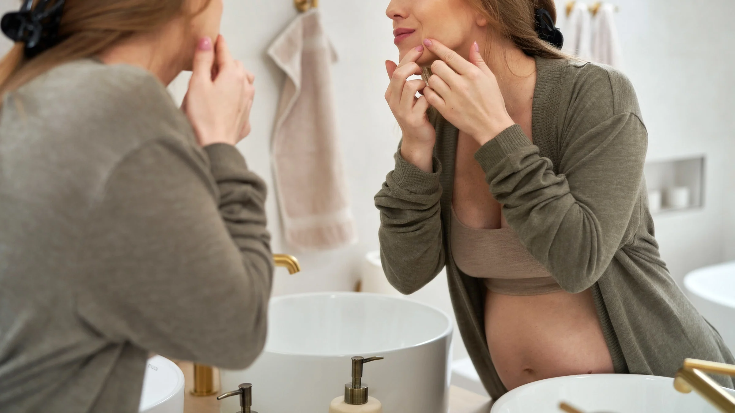 A pregnant person popping a pimple.