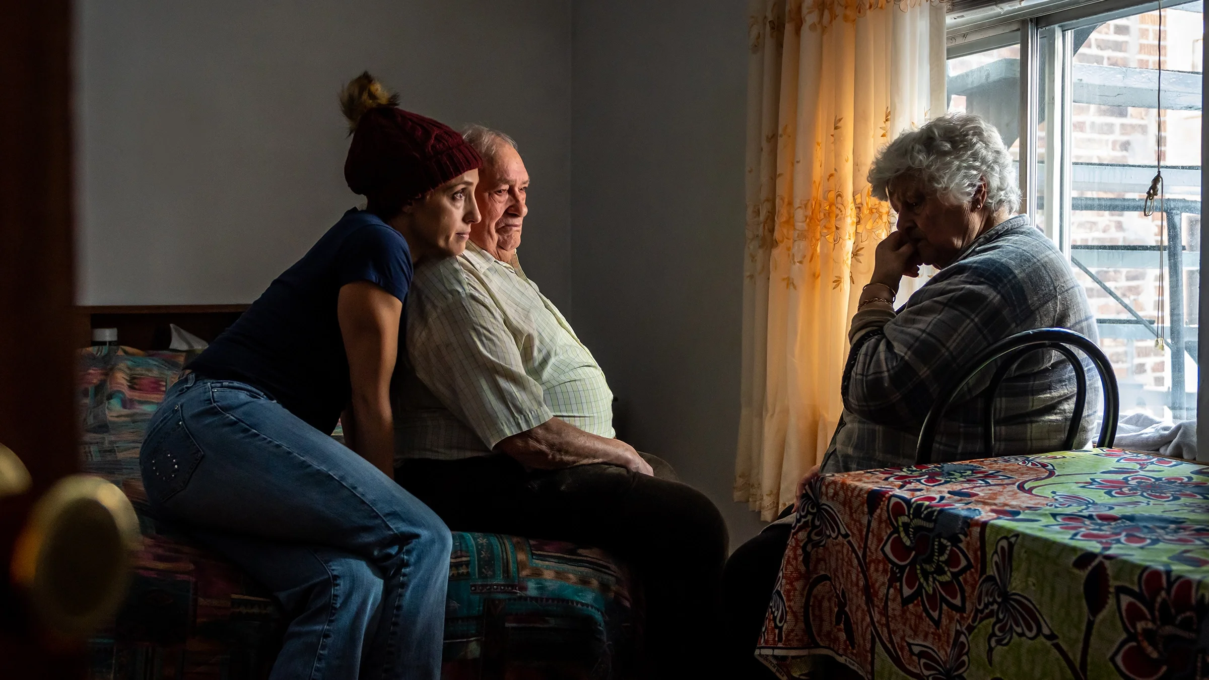 Portrait of an older couple talking with their daughter by a window in a room.