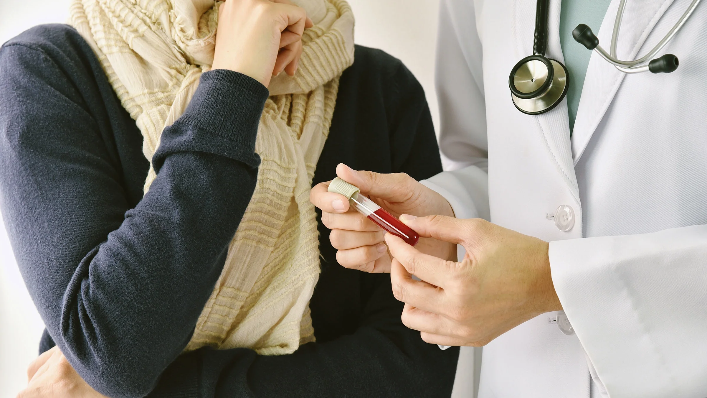 A doctor holding a blood vial, talking to a patient.