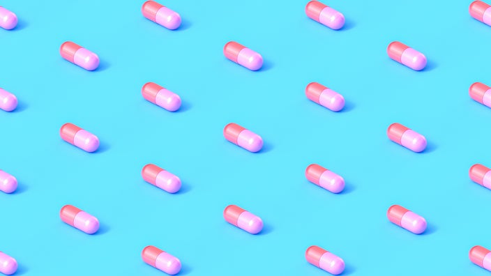 Red and pink capsule pills lined up in a diagonal pattern on a light blue background.