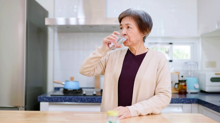 Senior woman takes medicine with a glass of water in the kitchen of her home.