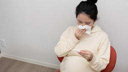A pregnant person blowing their nose and checking their temperature.
SasinParaksa/iStock via Getty Images Plus