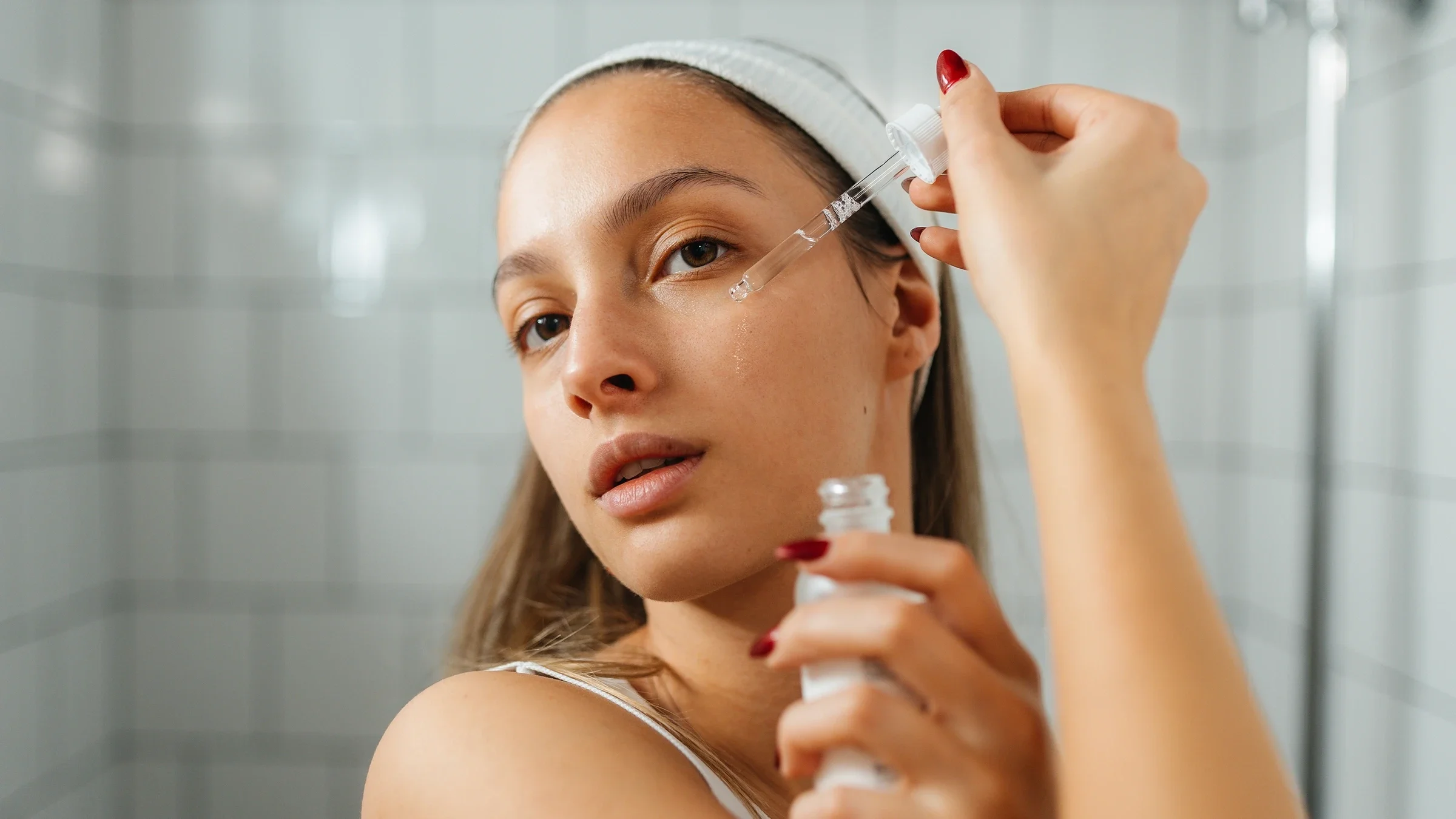 A woman applies oil to her face with a dropper.