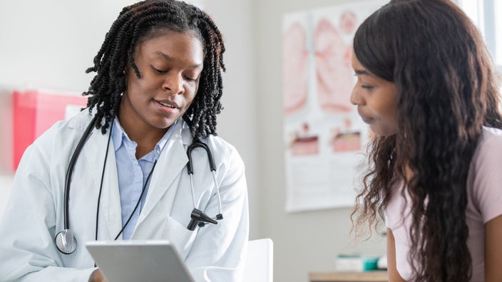 A healthcare professional uses a digital tablet while talking to a patient.