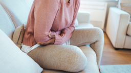 Cropped shot of a woman holding her stomach in pain as she rocks forward on the couch.
dragana991/iStock via Getty Images