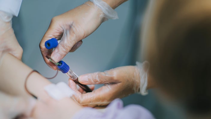 A close-up image shows a healthcare worker drawing blood.