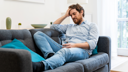 A tired man sits on a couch and drinks water.
Paolo Cordoni/iStock via Getty Images Plus 