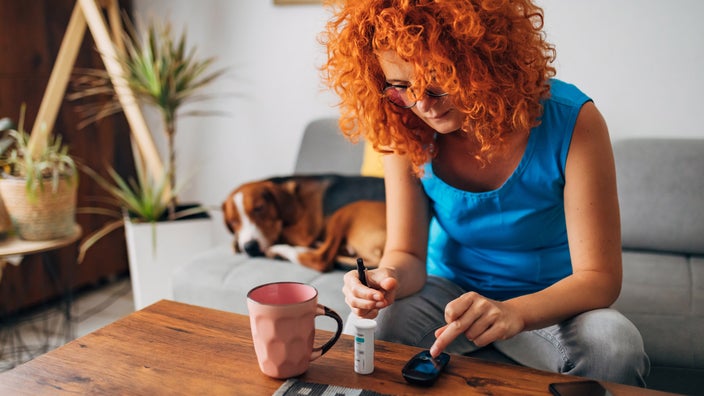 A person using their glucometer at a coffee table. Their dog is sleeping next to them.