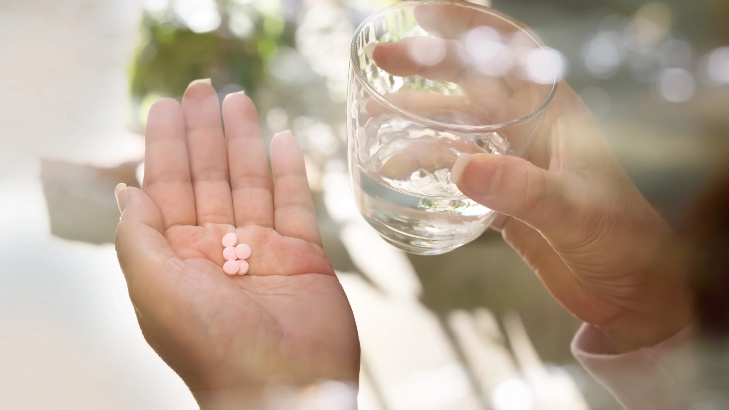 A person holding a glass of water and a hand full of supplements.