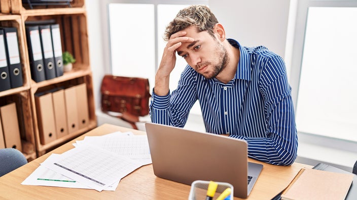 A man looks stressed while working on a laptop.