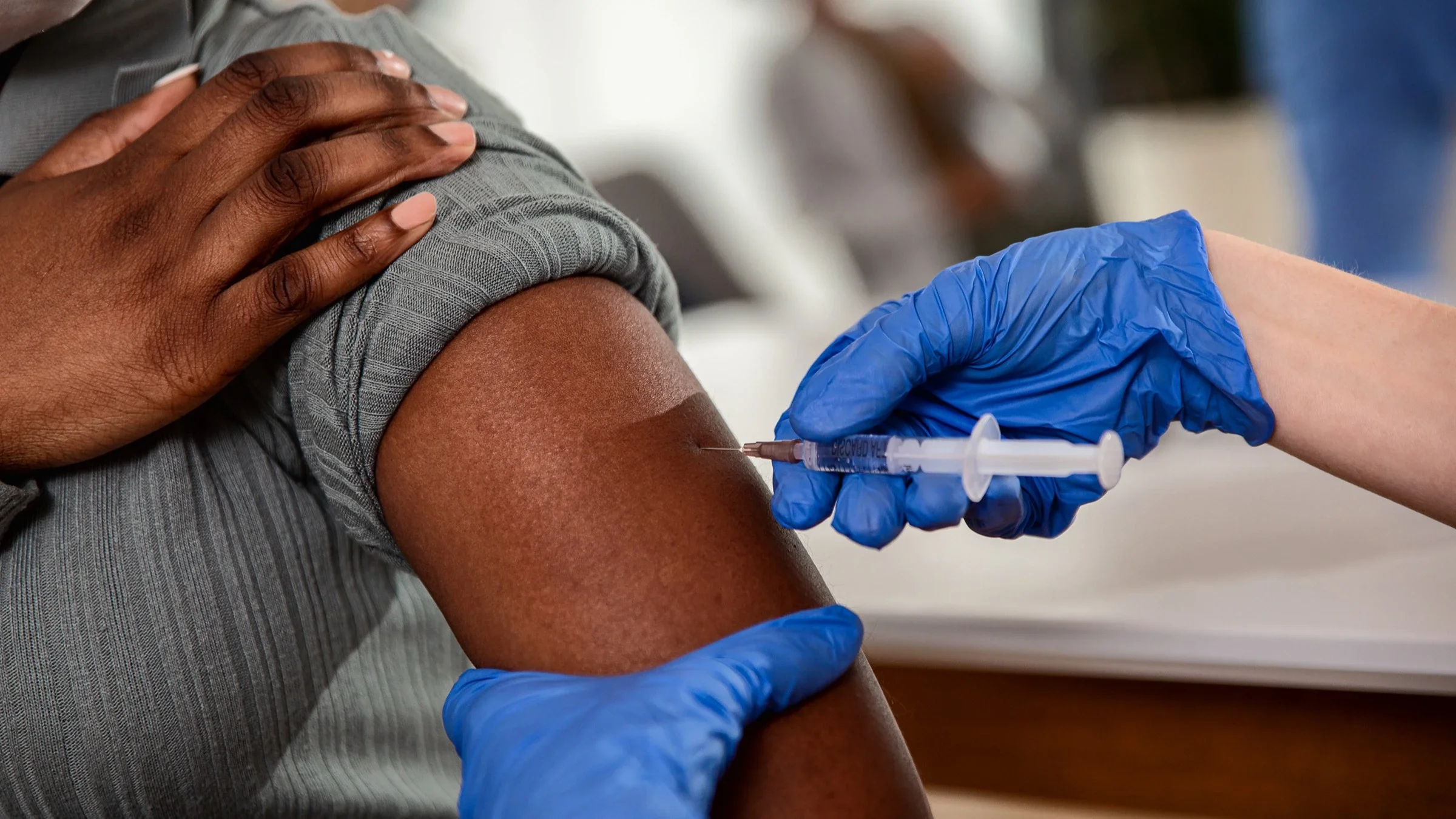Close-up of a nurse with blue medical gloves administering a vaccine.