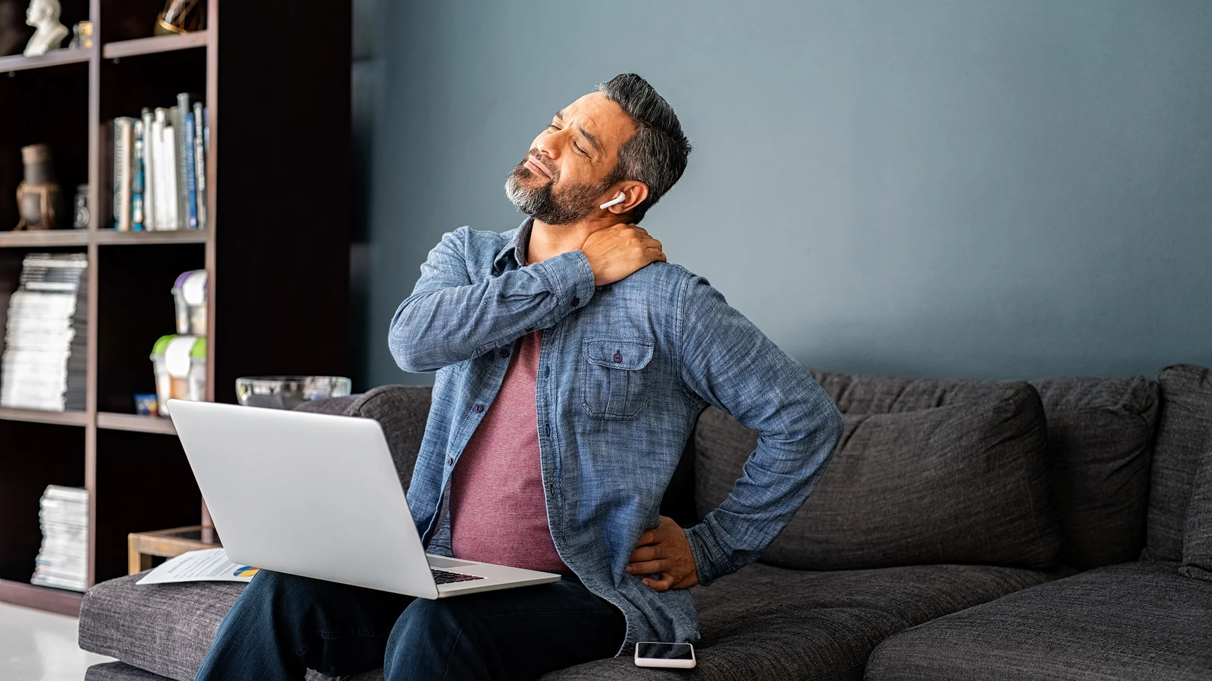 A person stretches their neck and back while sitting on a couch.