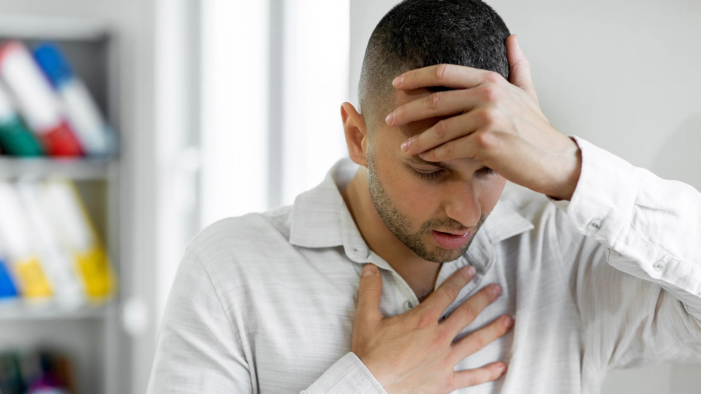 A man clutches his forehead and chest in discomfort as he struggles with breathing problem.