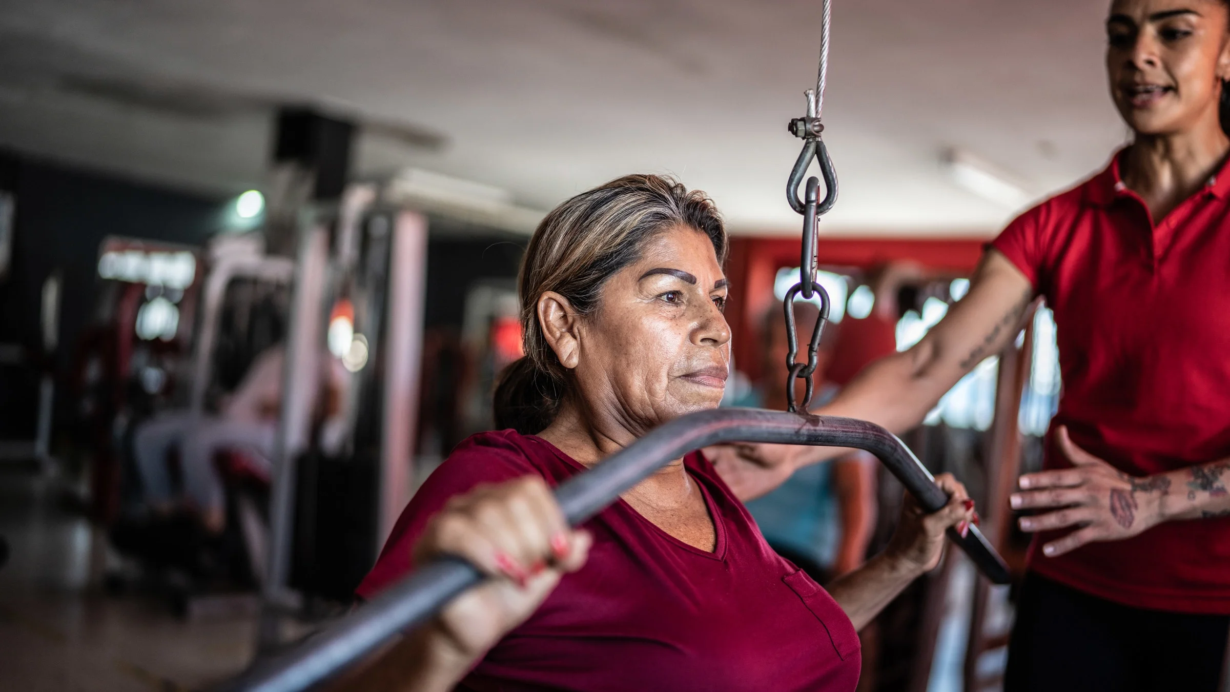 A trainer helping an older adult using a weight machine.
