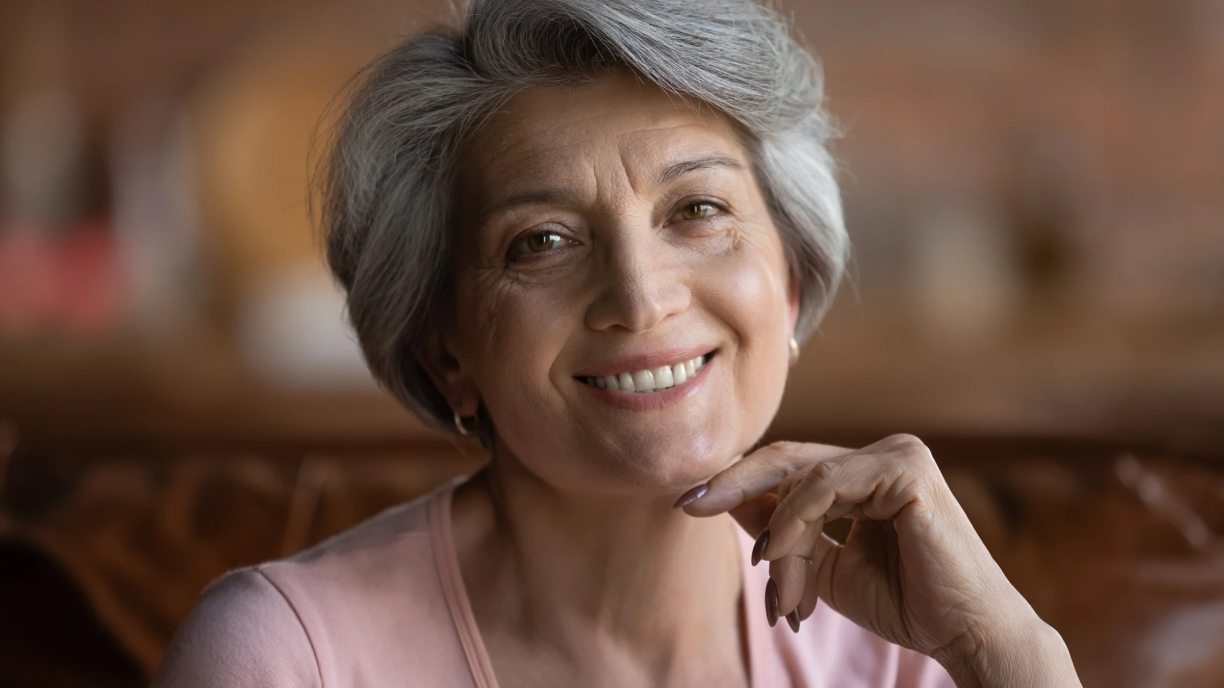 Close-up portrait of a senior woman smiling with her chin resting on her hand.