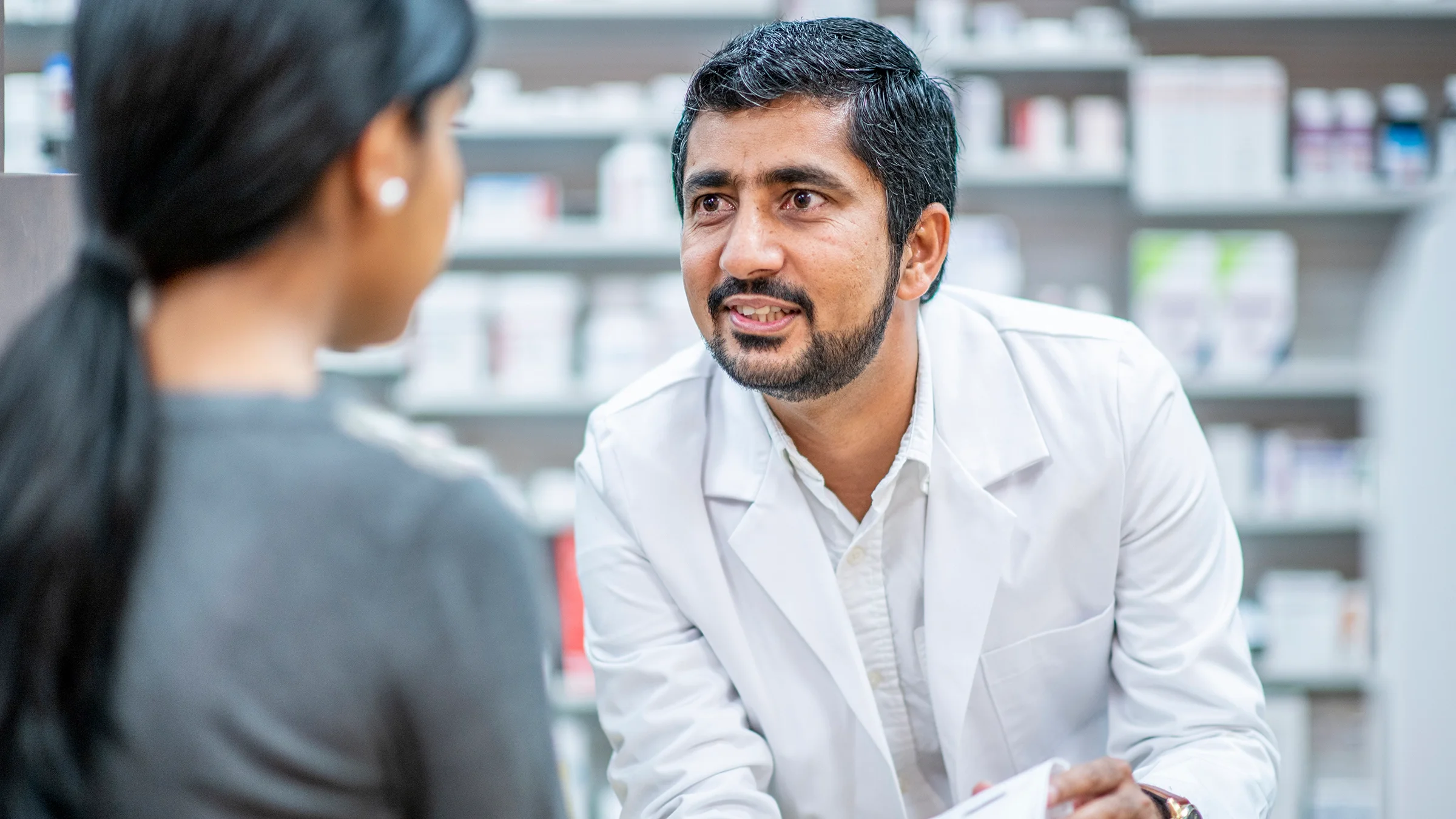 Pharmacist consulting with patient at counter.