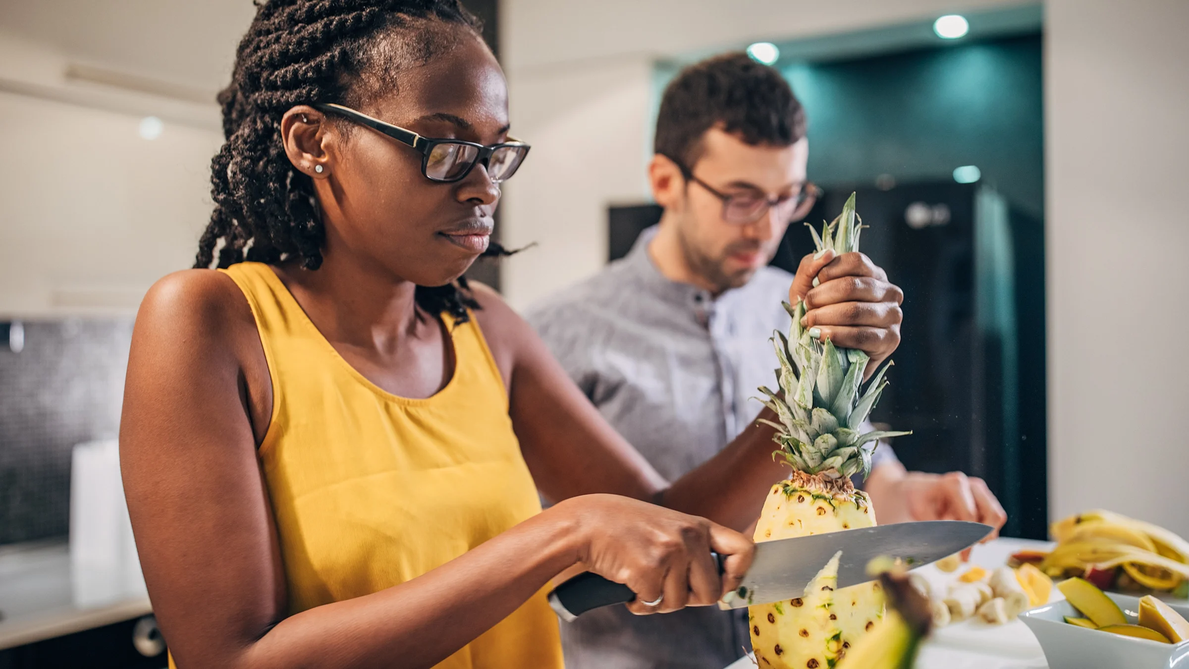 A woman is cutting pineapple in the kitchen.