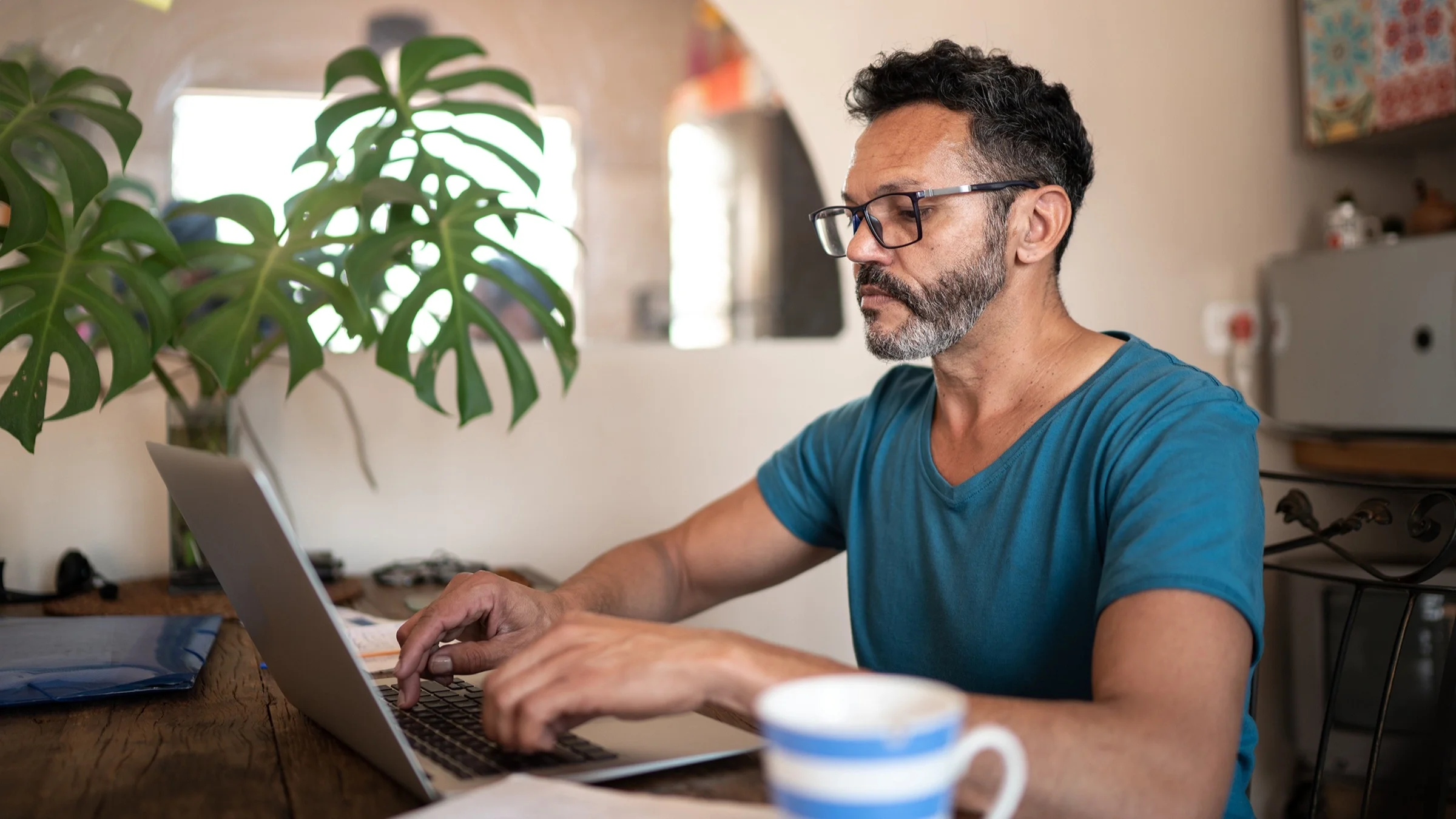 An adult is sitting at his dining table on his laptop. He has a very concentrated look on his face as he types.